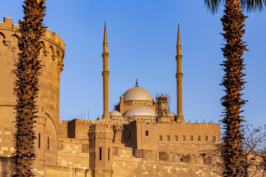 Salah El Din Citadel in Cairo, featuring tall minarets, domed roofs, and ancient stone walls at sunset.