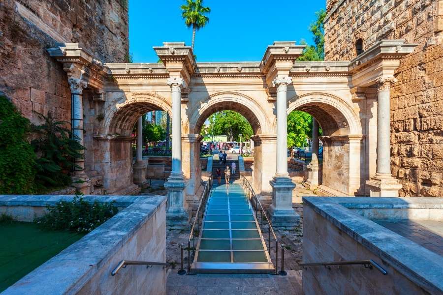 Historic Hadrian’s Gate in Antalya, featuring Roman arches, stone columns, and a modern glass walkway under bright daylight.