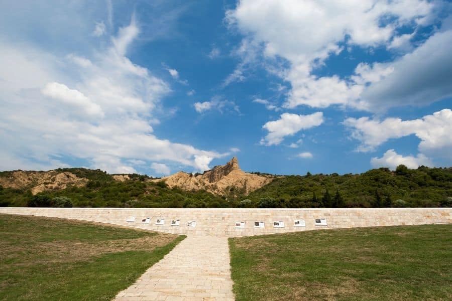 Memorial stone wall at Anzac Cove, Gallipoli, with plaques honoring fallen soldiers, set against rugged hills and a cloudy sky.