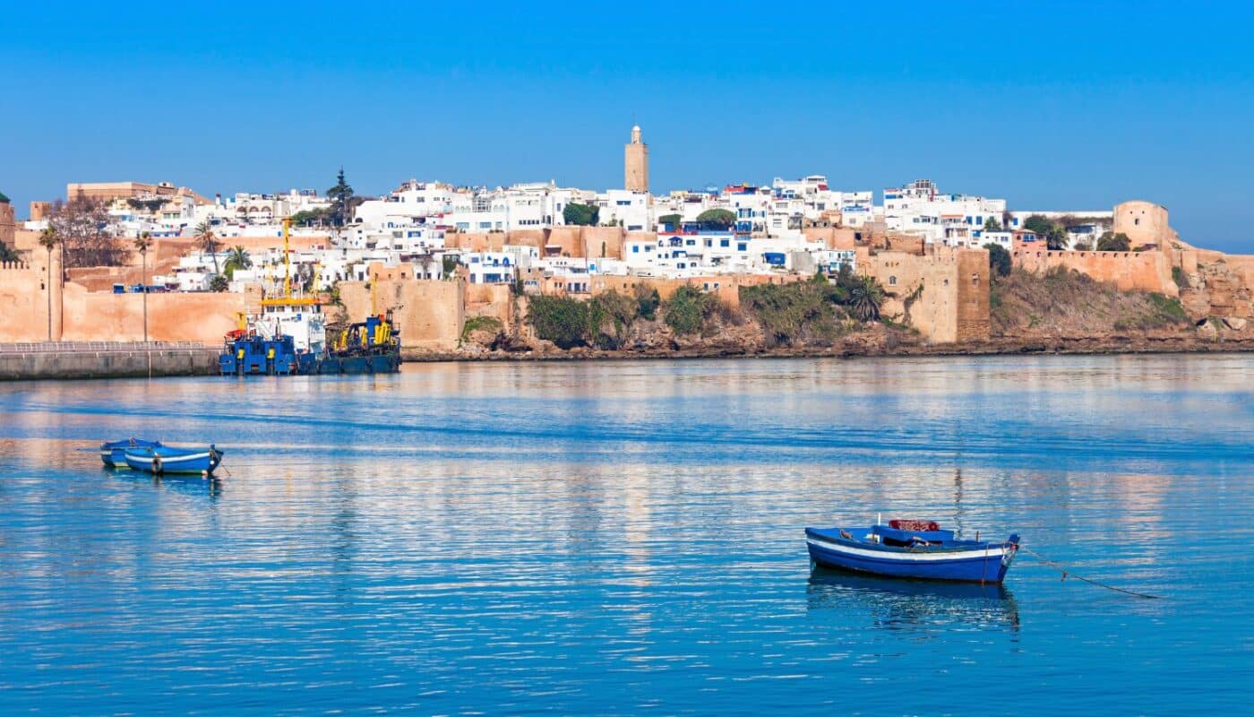 Coastal view of Rabat, Morocco, featuring the Kasbah of the Udayas and serene blue water with fishing boats in the foreground.
