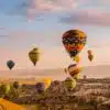 View of colorful hot air balloons flying over Cappadocia's unique landscapes, perfect for Turkey tours