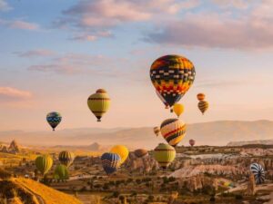 View of colorful hot air balloons flying over Cappadocia's unique landscapes, perfect for Turkey tours
