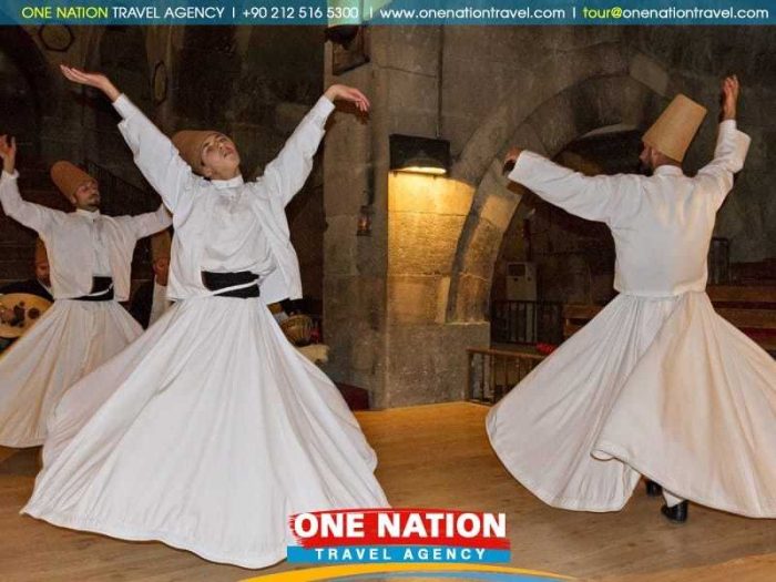 Three individuals performing a traditional Sufi whirling dance in long white robes and tall hats inside a historic building.