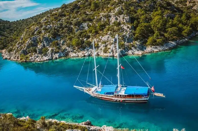 A sailboat is anchored near a rocky coastline with clear turquoise waters.