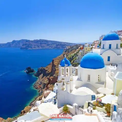 Breathtaking aerial view of Santorini Island featuring white-washed buildings with blue domes overlooking the Aegean Sea.