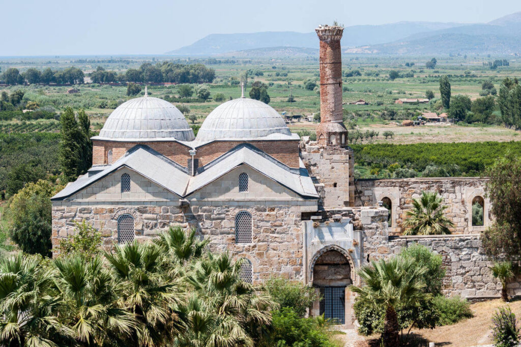 Historic Isabey Mosque with stone arches, ornate entrance, and Seljuk-style architecture under clear blue sky.