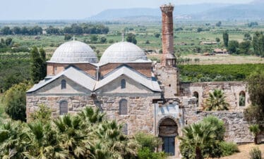 Historic Isabey Mosque with stone arches, ornate entrance, and Seljuk-style architecture under clear blue sky.