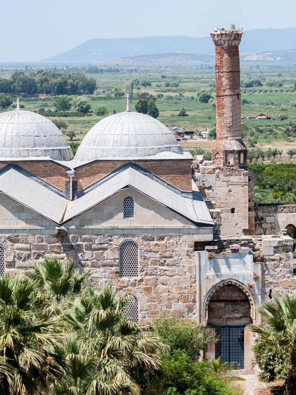 Historic Isabey Mosque with stone arches, ornate entrance, and Seljuk-style architecture under clear blue sky.