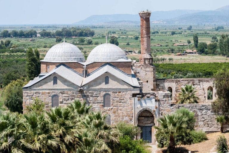 Historic Isabey Mosque with stone arches, ornate entrance, and Seljuk-style architecture under clear blue sky.