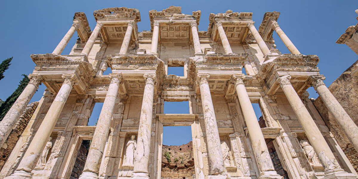 Imposing marble facade of the Celsus Library in Ephesus, with tall Corinthian columns and carved statues under a clear sky.