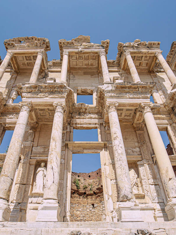 Imposing marble facade of the Celsus Library in Ephesus, with tall Corinthian columns and carved statues under a clear sky.