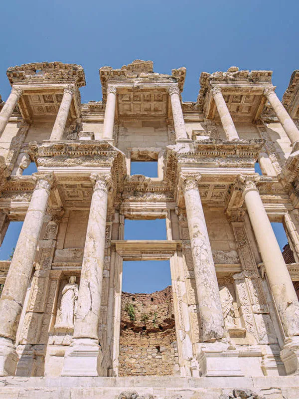 Imposing marble facade of the Celsus Library in Ephesus, with tall Corinthian columns and carved statues under a clear sky.