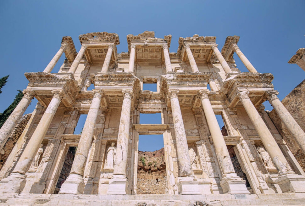 Imposing marble facade of the Celsus Library in Ephesus, with tall Corinthian columns and carved statues under a clear sky.