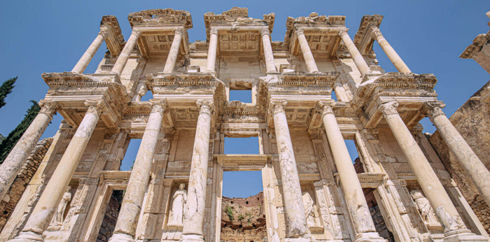 Imposing marble facade of the Celsus Library in Ephesus, with tall Corinthian columns and carved statues under a clear sky.