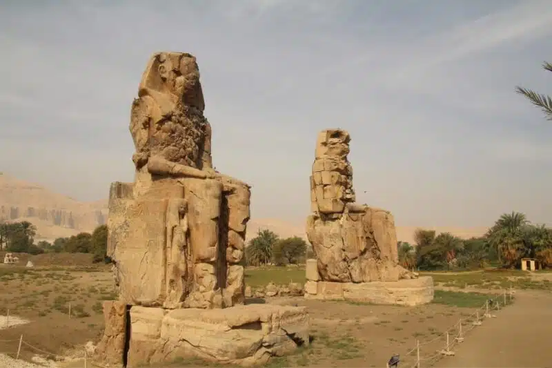 Majestic Colossi of Memnon statues standing tall in Luxor, Egypt, against a clear blue sky.