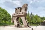 Wooden Trojan Horse sculpture, exterior view, with intricate carvings and large hollow body, set against a clear sky.