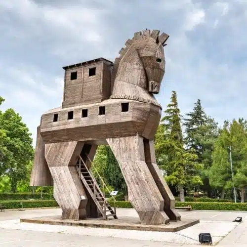 Wooden Trojan Horse sculpture, exterior view, with intricate carvings and large hollow body, set against a clear sky.