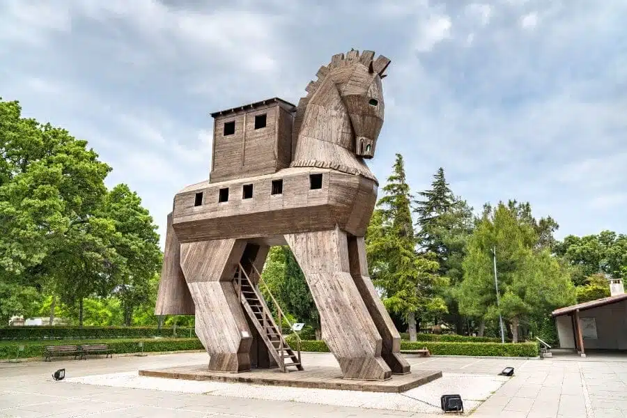 Wooden Trojan Horse sculpture, exterior view, with intricate carvings and large hollow body, set against a clear sky.