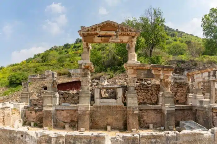 Ancient Fountain of Trajan in Ephesus, Turkey, featuring intricate Roman-era stonework and columns, surrounded by historical ruins.