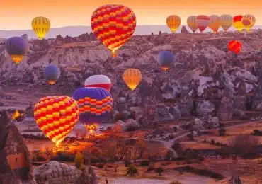 Scenic view of colorful hot air balloons over Cappadocia's unique rock formations at sunrise.