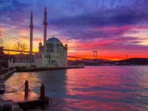 Ortakoy Mosque and Bosphorus Bridge at sunset with orange sky backdrop.