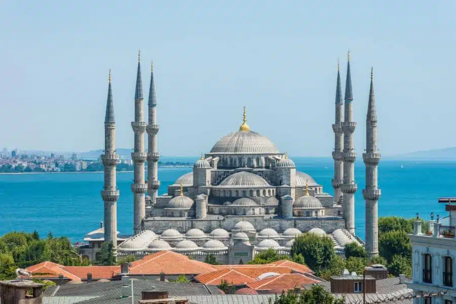 Aerial view of the Sultanahmet Mosque with its domes and minarets, surrounded by the cityscape and a stunning sea view in the background.