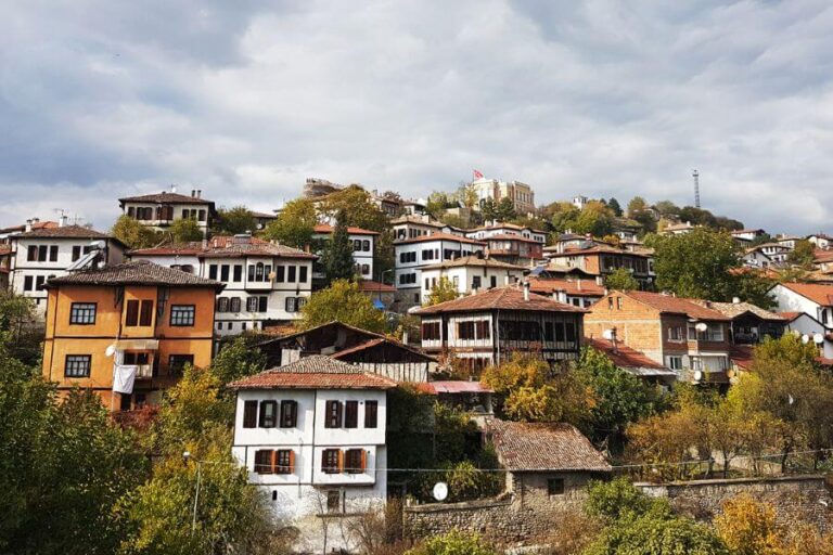 Traditional Ottoman-style Safranbolu houses with white facades, red-tiled roofs, and wooden details, nestled on a hillside.