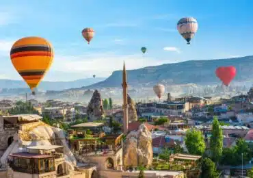 Hot air balloon floating over a mosque in Goreme at sunrise, showcasing Cappadocia's stunning landscape.