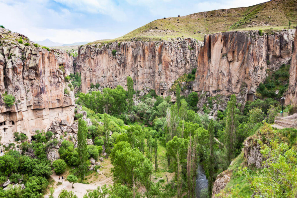 Lush green trees and a winding stream between steep rocky cliffs in Ihlara Valley, Cappadocia, Turkey.