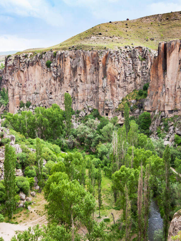 Lush green trees and a winding stream between steep rocky cliffs in Ihlara Valley, Cappadocia, Turkey.