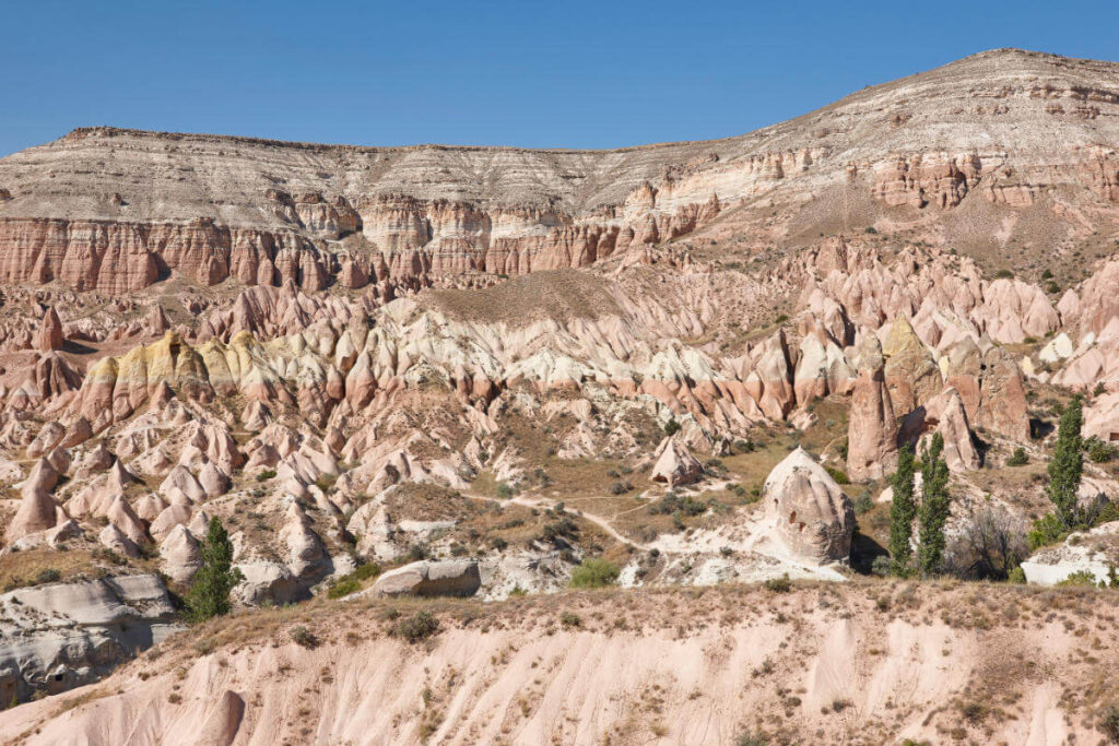 Eroded red rock formations in Cappadocia's Red Valley under soft daylight with rugged cliffs and unique terrain.