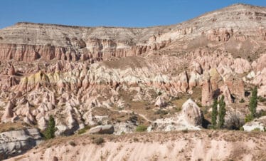 Eroded red rock formations in Cappadocia's Red Valley under soft daylight with rugged cliffs and unique terrain.