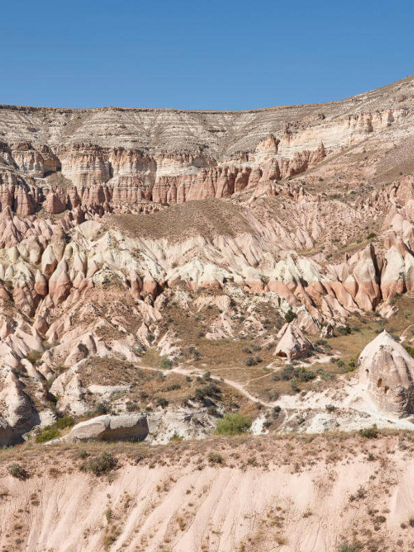 Eroded red rock formations in Cappadocia's Red Valley under soft daylight with rugged cliffs and unique terrain.