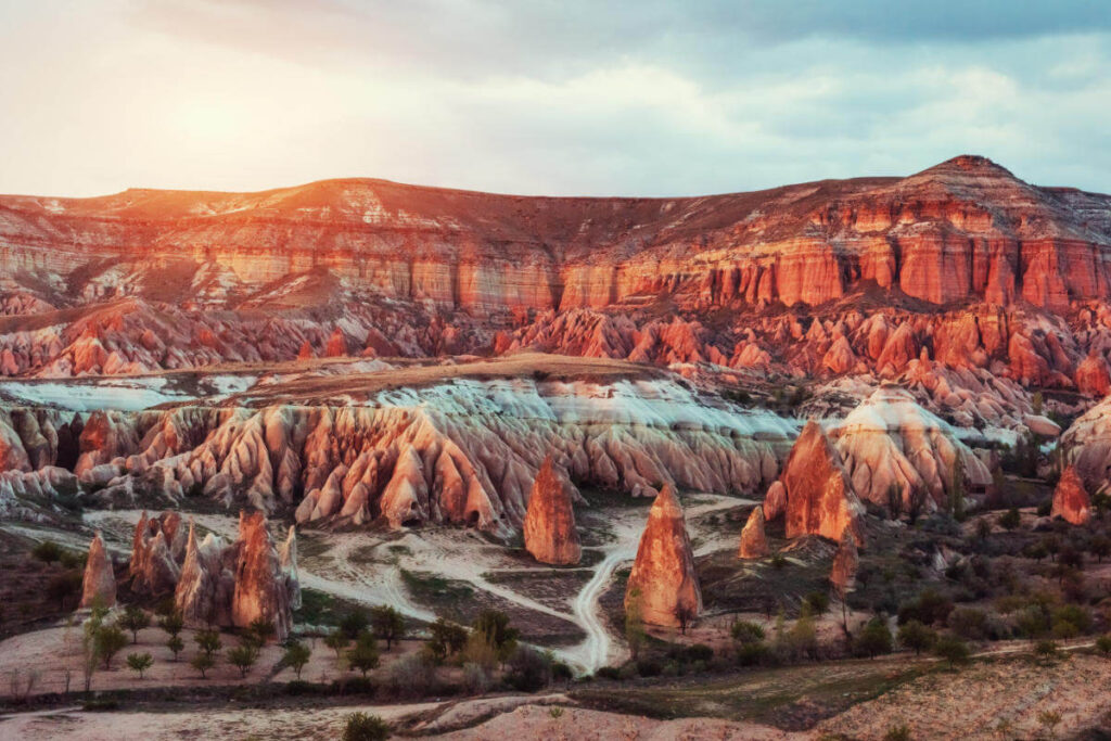 Vibrant sunset casting warm light over Red Valley's rugged rock formations in Cappadocia, Turkey.