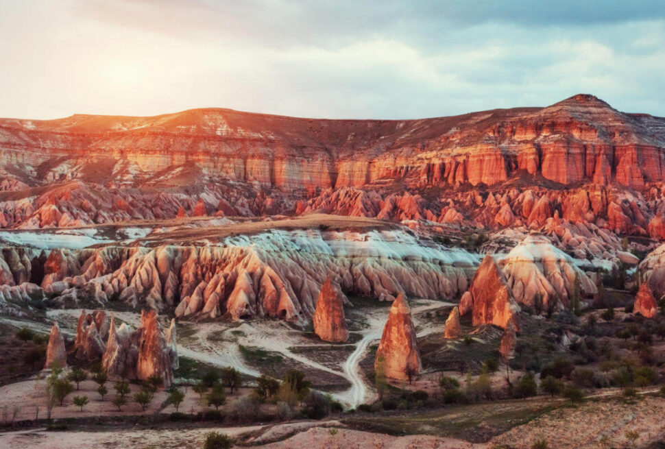 Vibrant sunset casting warm light over Red Valley's rugged rock formations in Cappadocia, Turkey.