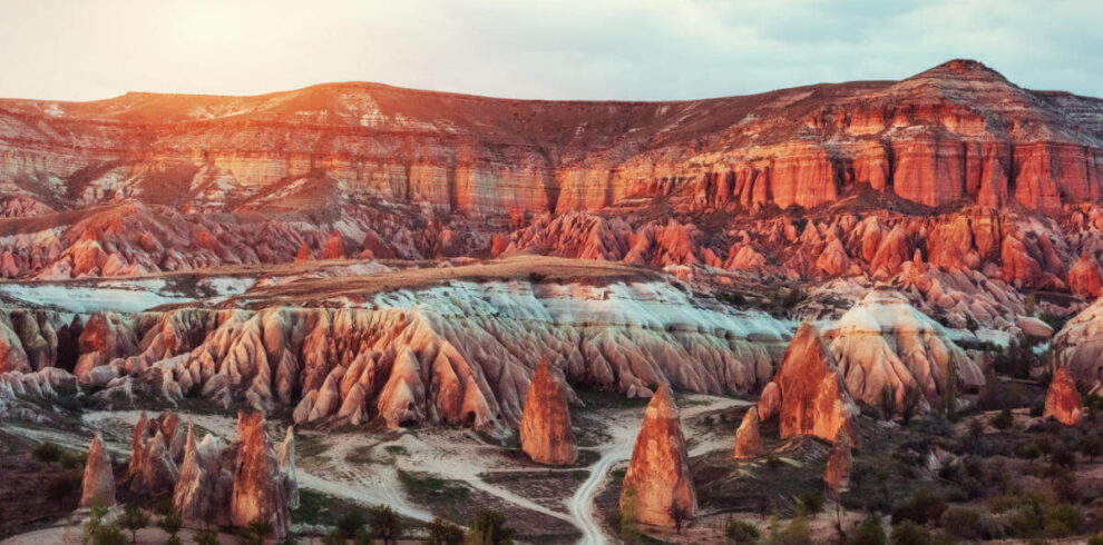 Vibrant sunset casting warm light over Red Valley's rugged rock formations in Cappadocia, Turkey.