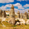 Tall, phallic-shaped fairy chimneys in Love Valley, Cappadocia, under a bright blue sky with scattered clouds.