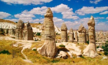 Tall, phallic-shaped fairy chimneys in Love Valley, Cappadocia, under a bright blue sky with scattered clouds.