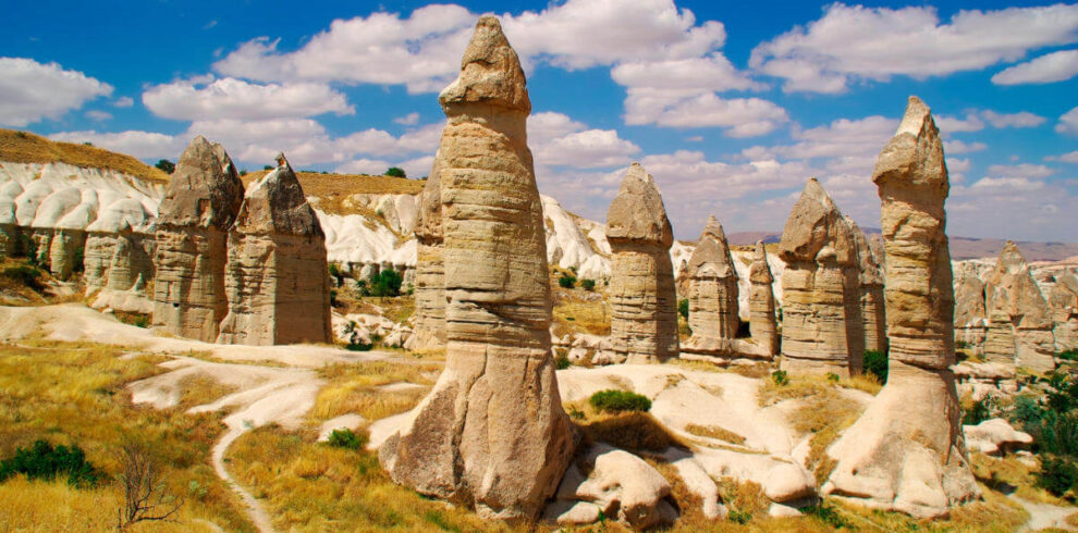 Tall, phallic-shaped fairy chimneys in Love Valley, Cappadocia, under a bright blue sky with scattered clouds.