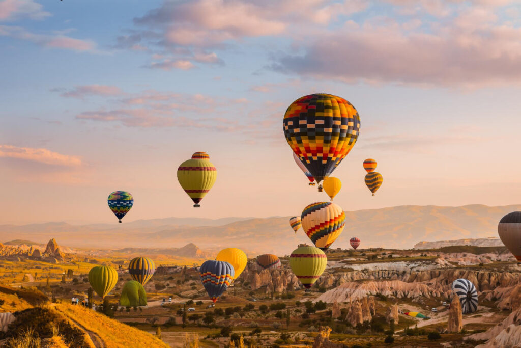Colorful hot air balloons rise over Cappadocia’s rocky valleys at sunrise, creating a stunning aerial view of the landscape.