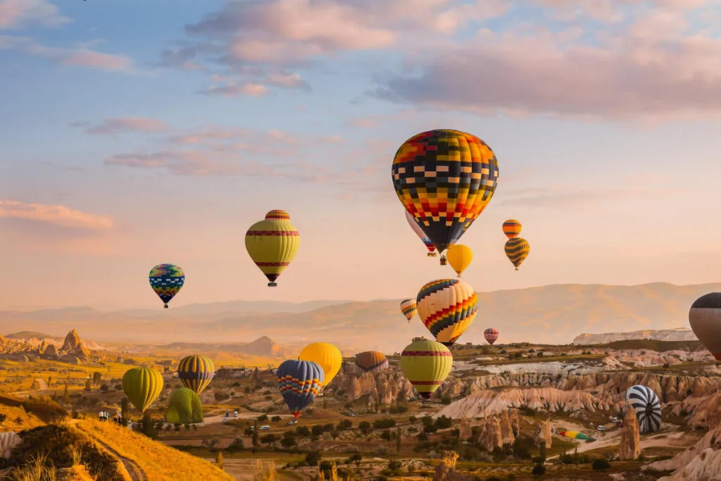 Colorful hot air balloons rise over Cappadocia’s rocky valleys at sunrise, creating a stunning aerial view of the landscape.