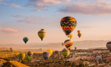 Colorful hot air balloons rise over Cappadocia’s rocky valleys at sunrise, creating a stunning aerial view of the landscape.