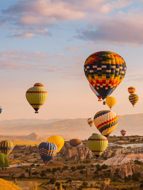 Colorful hot air balloons rise over Cappadocia’s rocky valleys at sunrise, creating a stunning aerial view of the landscape.