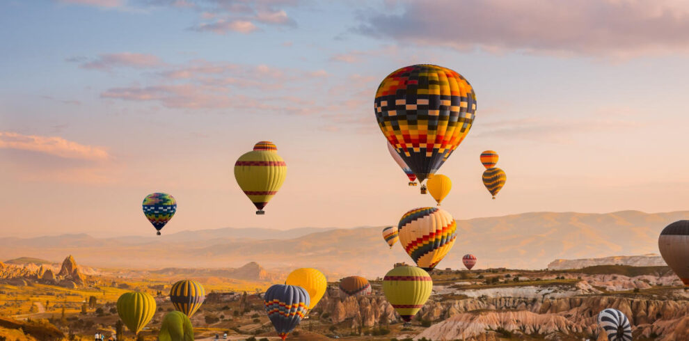 Colorful hot air balloons rise over Cappadocia’s rocky valleys at sunrise, creating a stunning aerial view of the landscape.