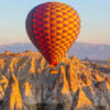 Colorful hot air balloon soaring above Cappadocia's rocky fairy chimneys at sunrise in Nevşehir, Turkey.