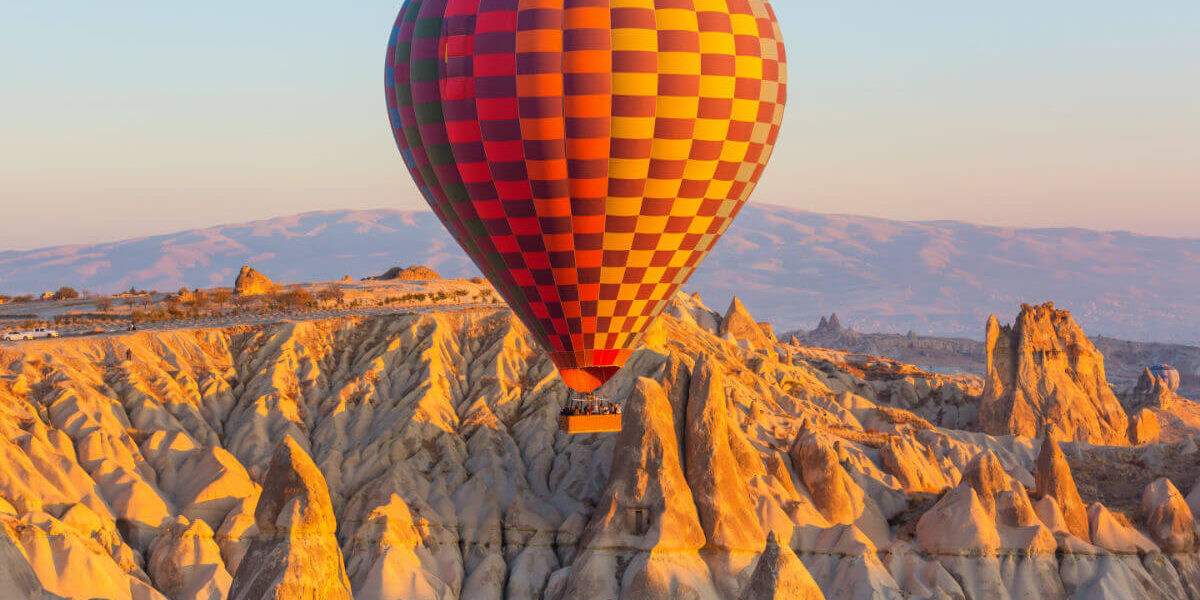 Colorful hot air balloon soaring above Cappadocia's rocky fairy chimneys at sunrise in Nevşehir, Turkey.