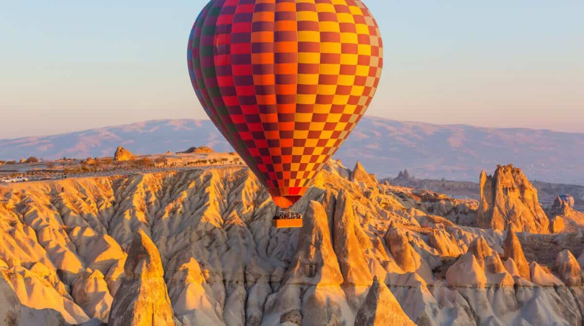 Colorful hot air balloon soaring above Cappadocia's rocky fairy chimneys at sunrise in Nevşehir, Turkey.