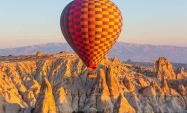 Colorful hot air balloon soaring above Cappadocia's rocky fairy chimneys at sunrise in Nevşehir, Turkey.