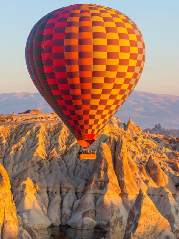 Colorful hot air balloon soaring above Cappadocia's rocky fairy chimneys at sunrise in Nevşehir, Turkey.