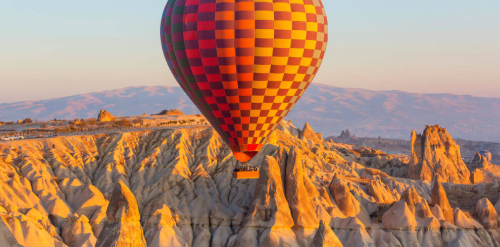 Colorful hot air balloon soaring above Cappadocia's rocky fairy chimneys at sunrise in Nevşehir, Turkey.